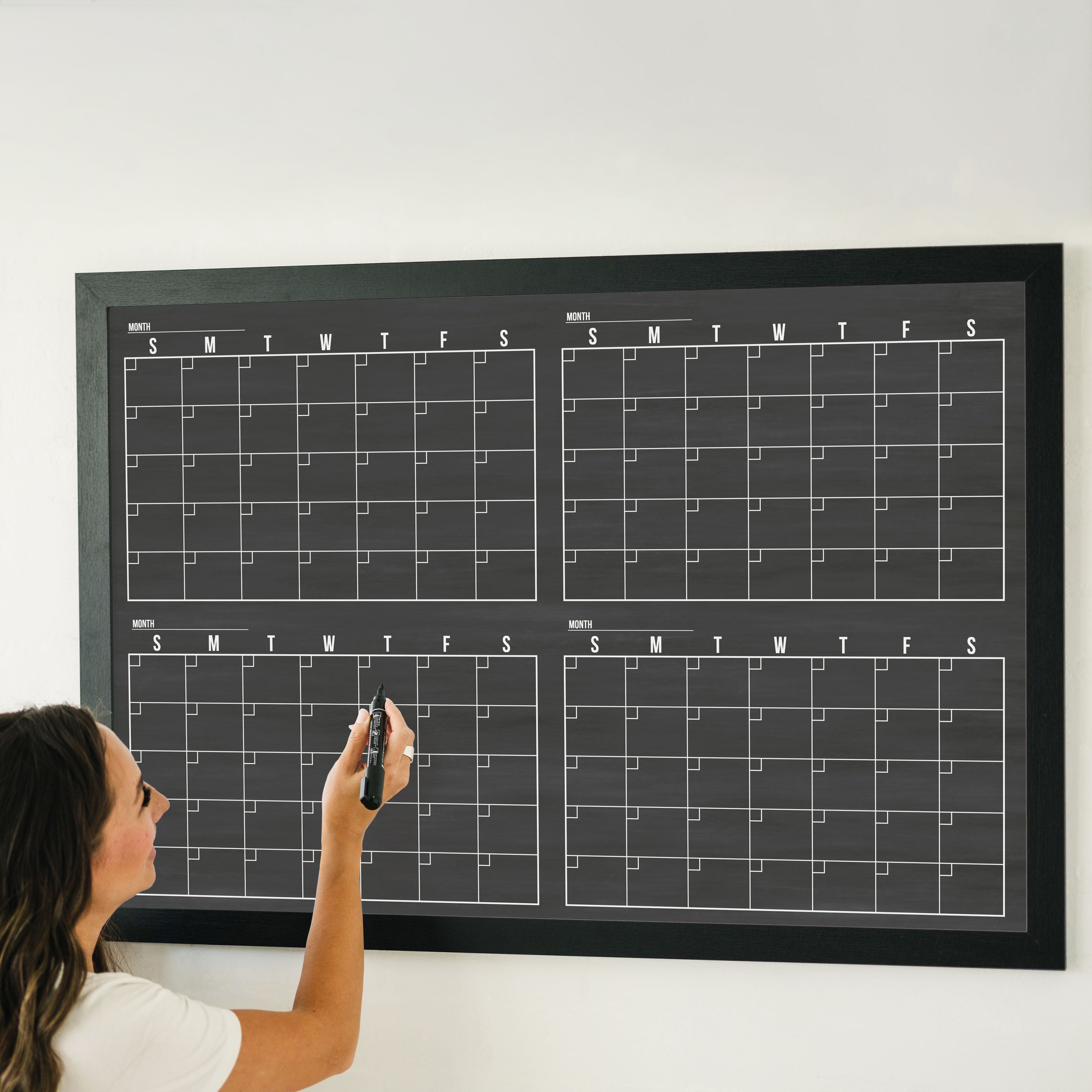 A framed dry-erase four month calendar with a chalkboard look hanging on the wall