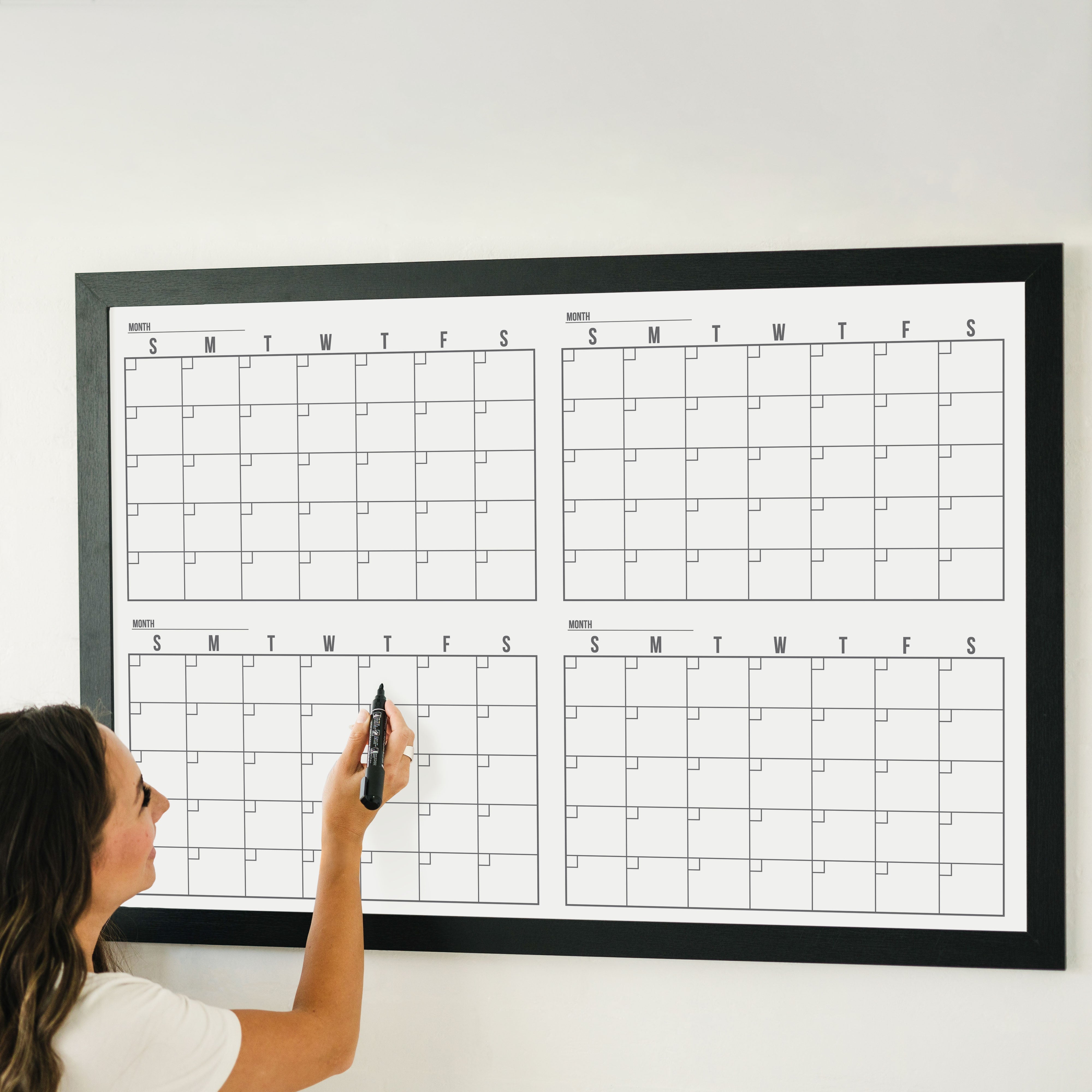 A framed whiteboard four month calendar hanging on the wall