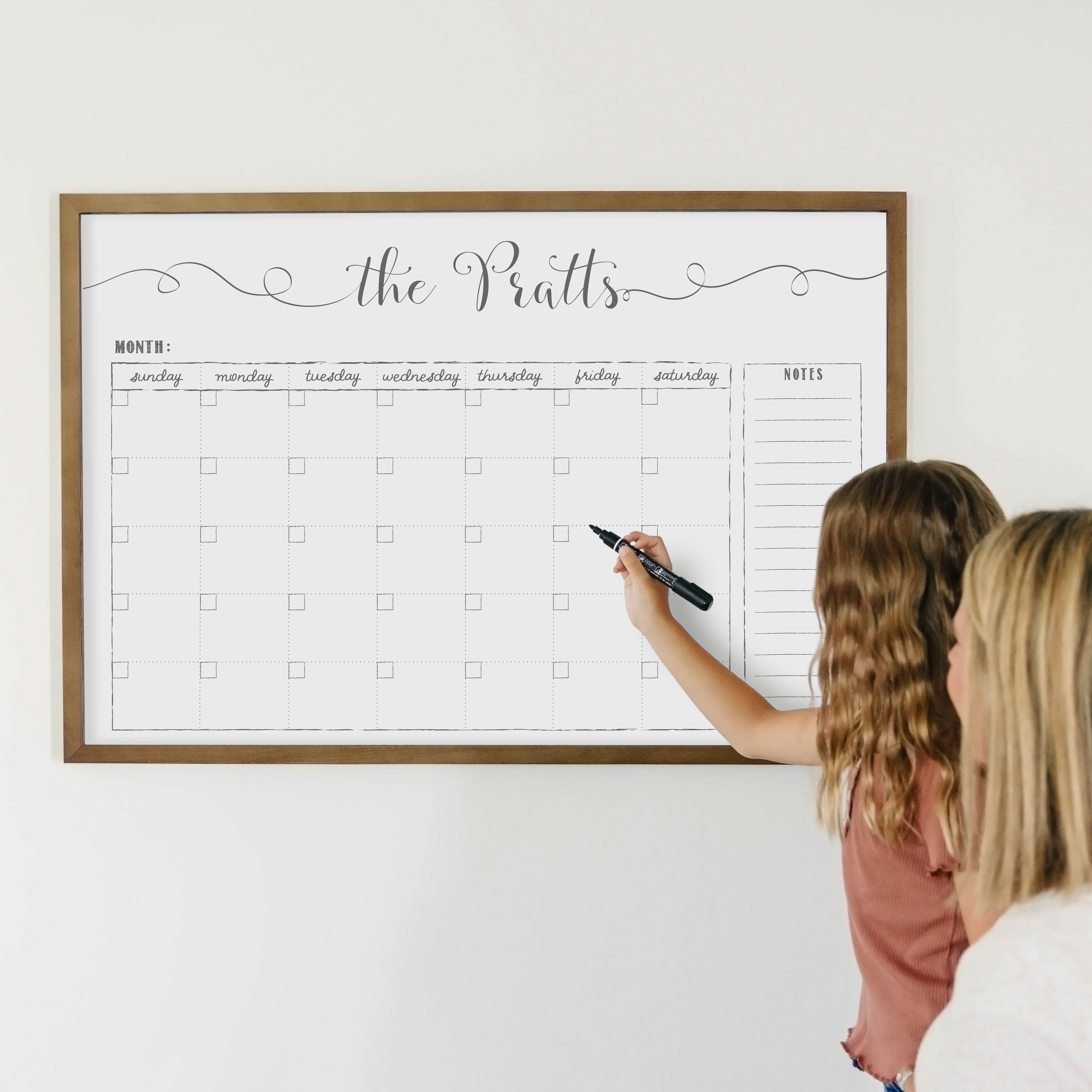 A framed whiteboard monthly calender hanging on the wall