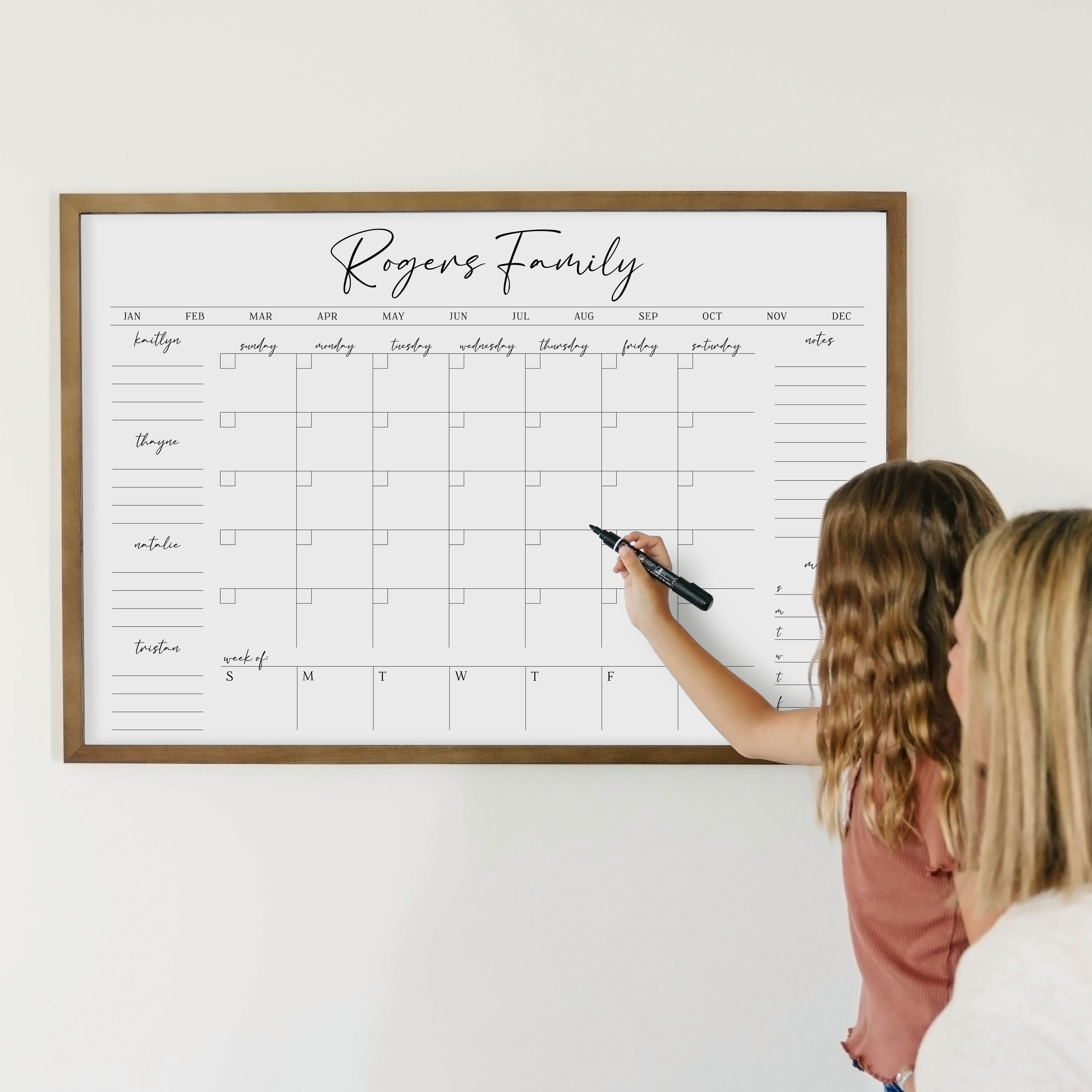 A framed whiteboard calendar with a monthly and weekly format hanging on the wall