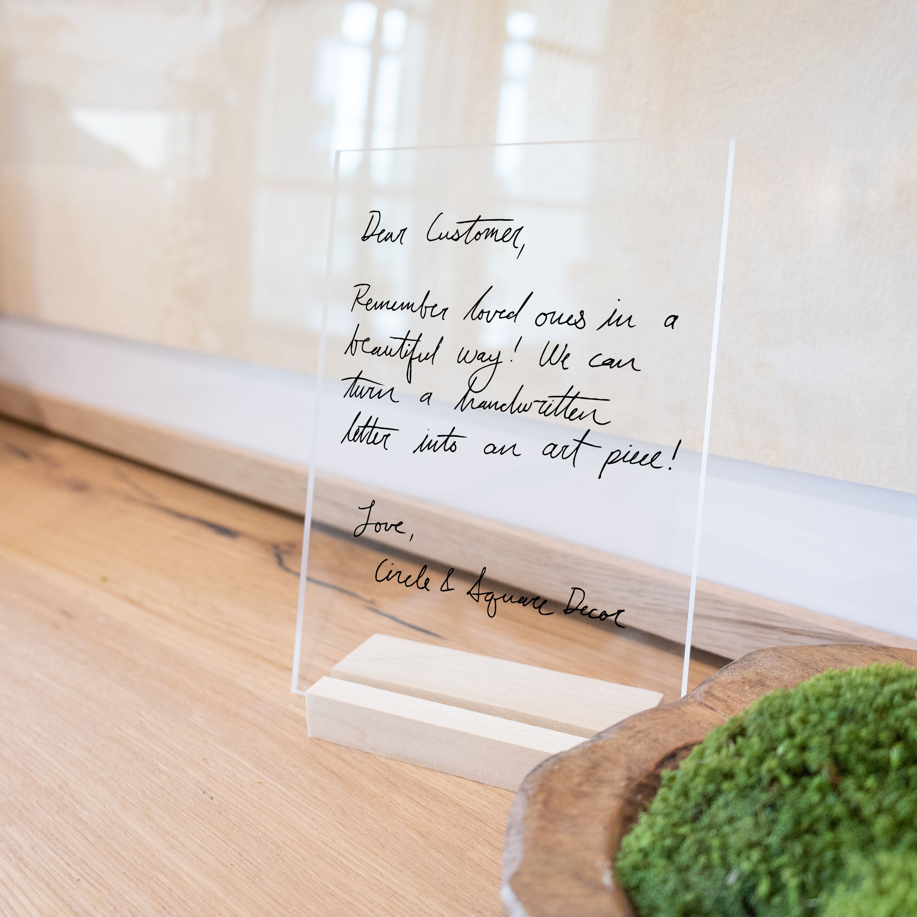 A handwriting memorial keepsake on clear acrylic with a blonde wooden stand. 