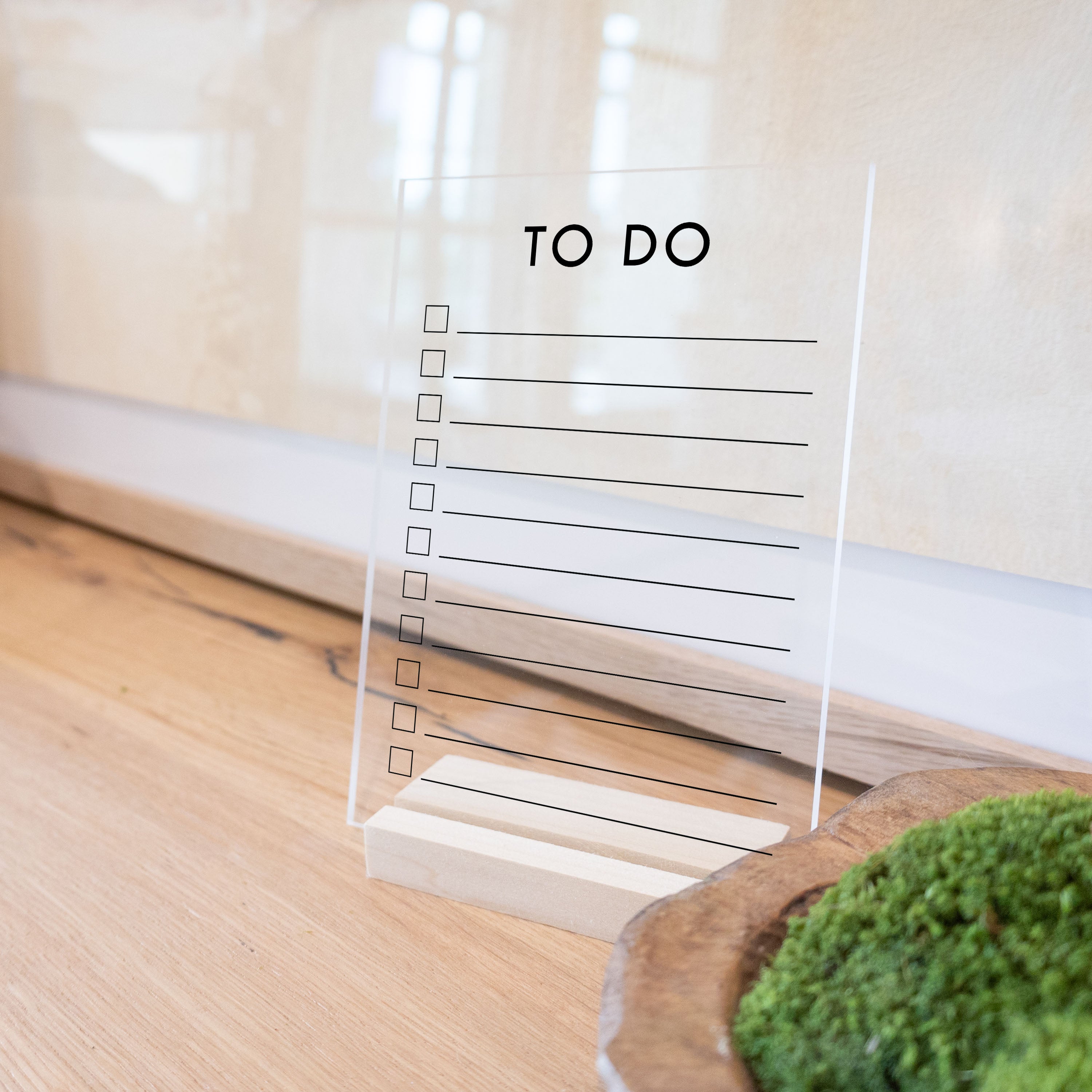 A minimalist to do list printed on clear acrylic with a wooden stand.