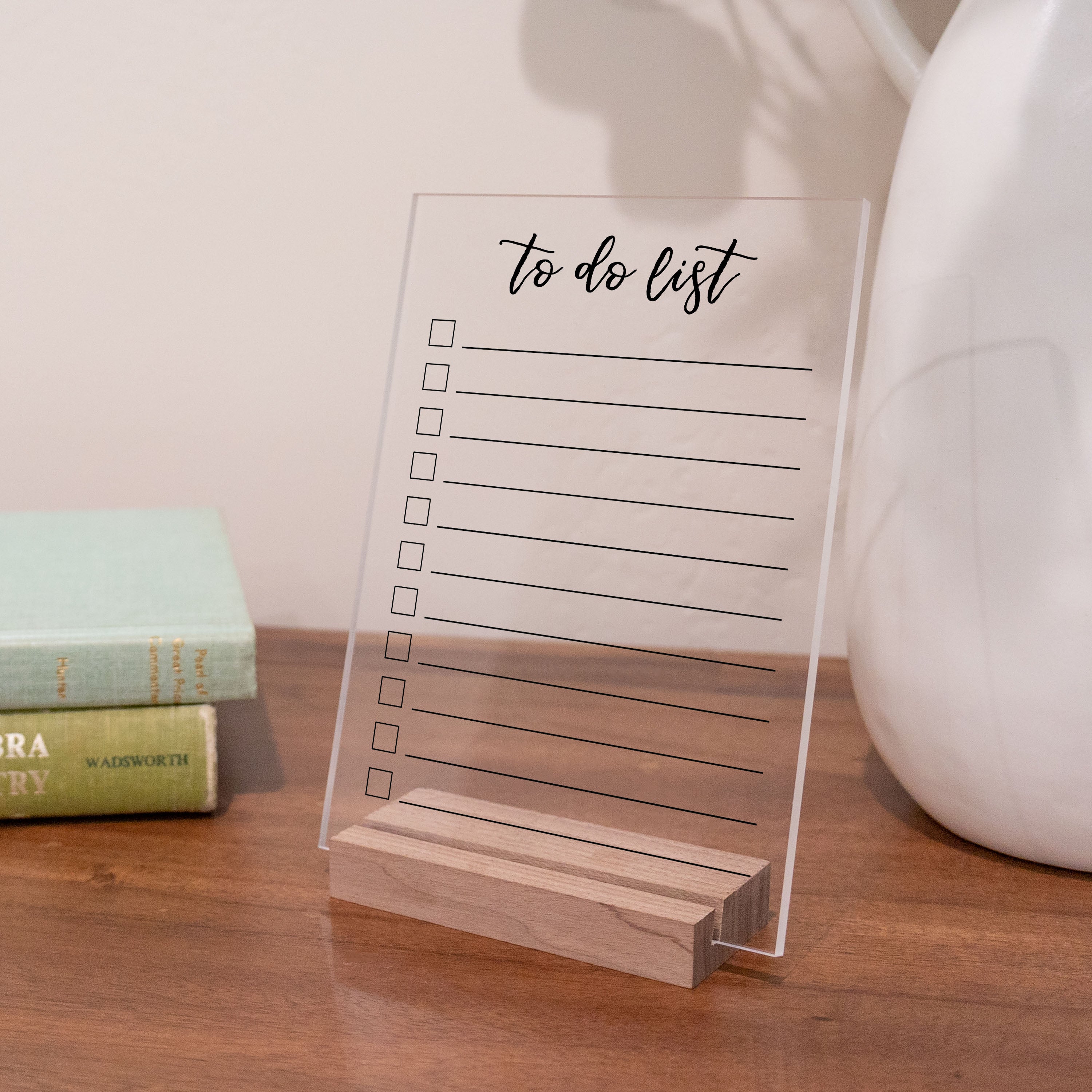 A to do list with a cursive title printed on clear acrylic on a nightstand. 