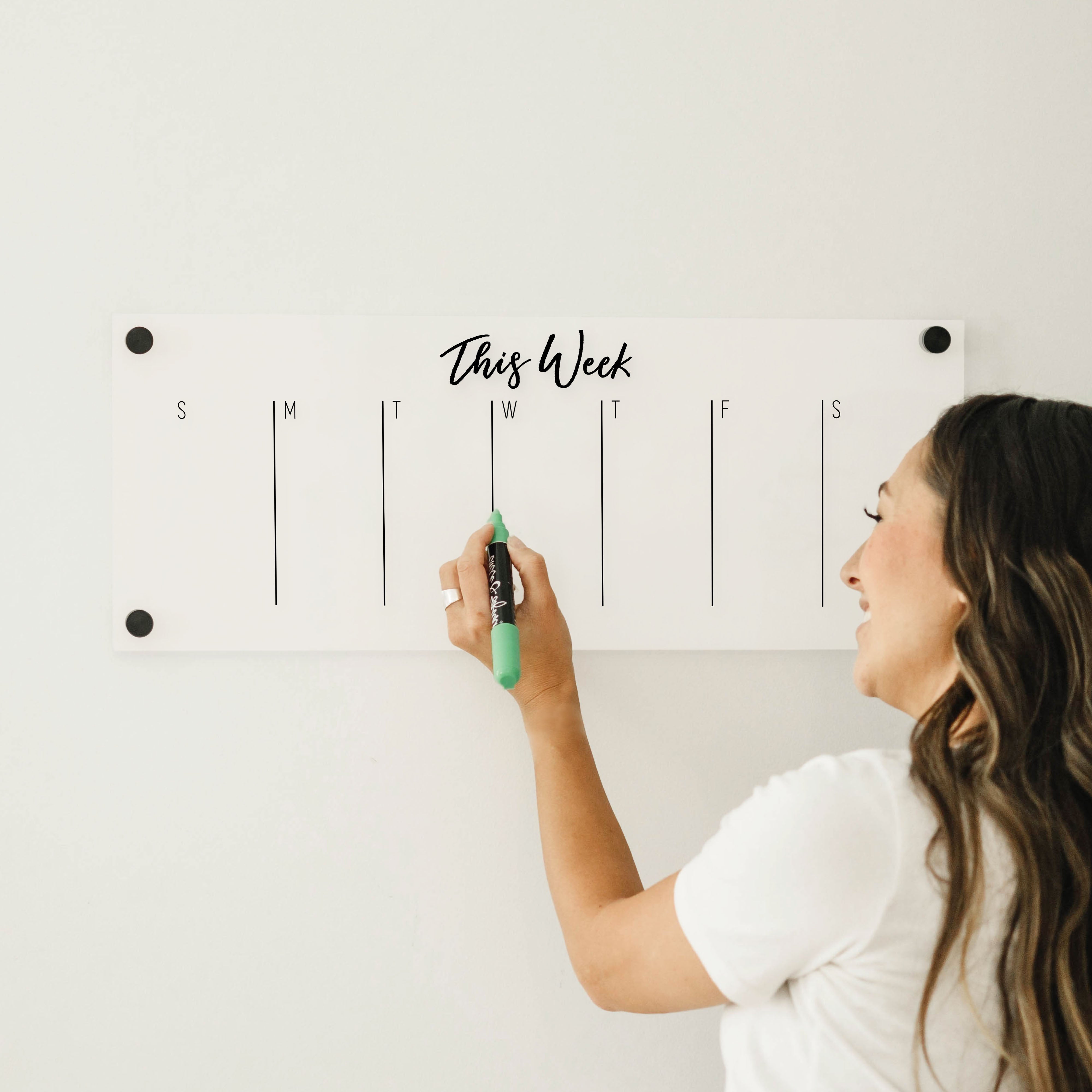 A skinny dry-erase weekly calender made of acrylic hanging on the wall