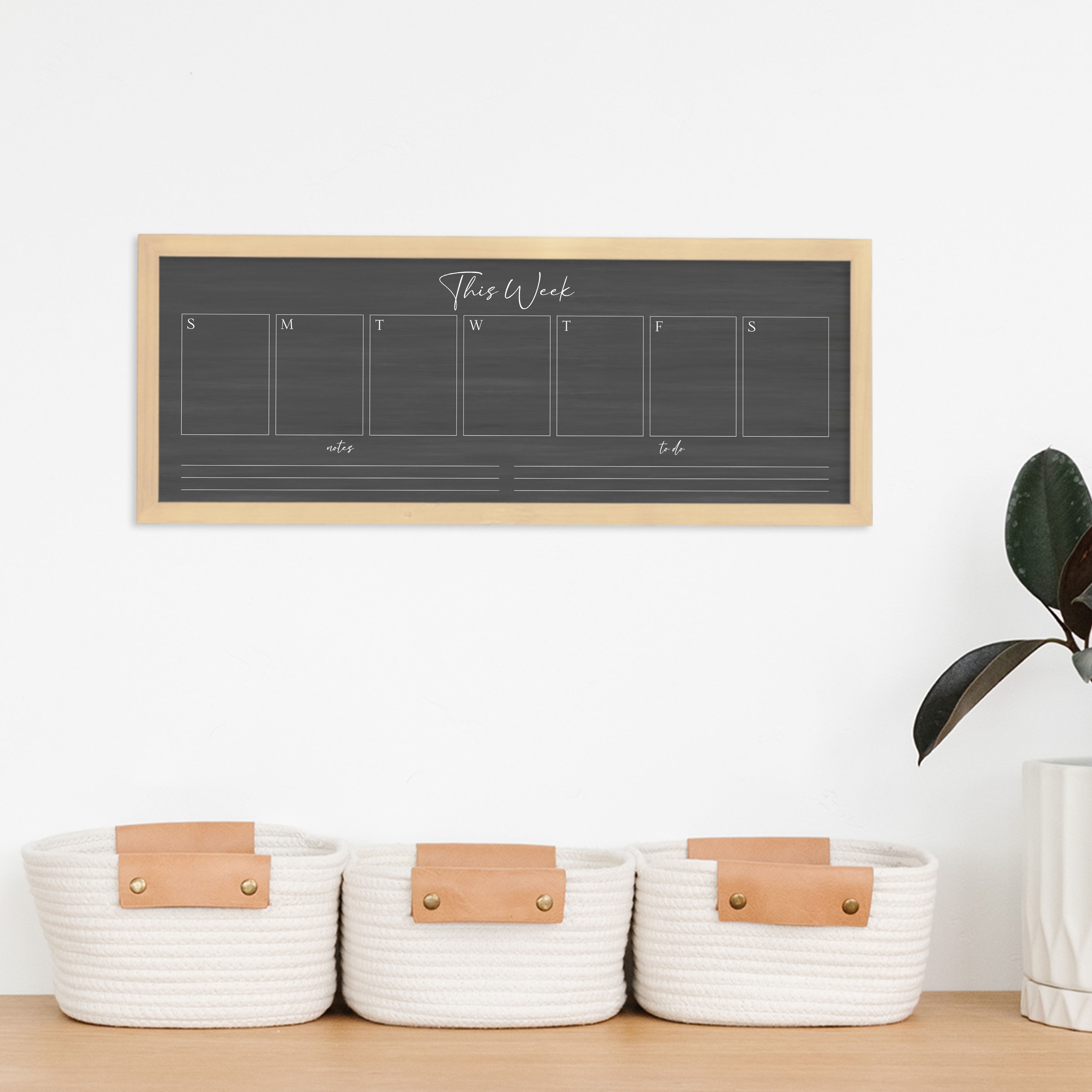 A framed slim dry-erase weekly calender with a faux chalkboard look hanging on the wall