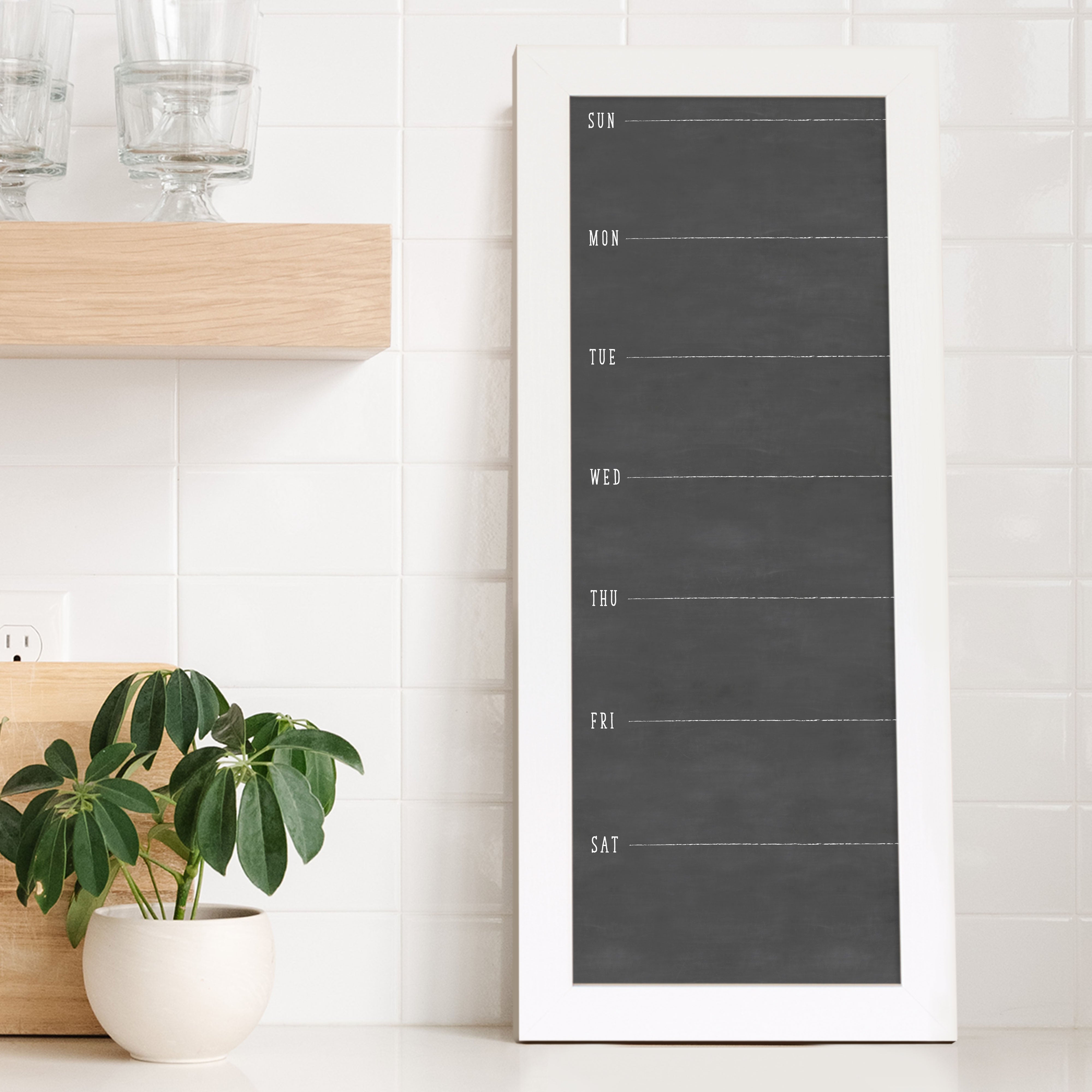 A framed slim dry-erase weekly calender with a faux chalkboard look hanging on the wall