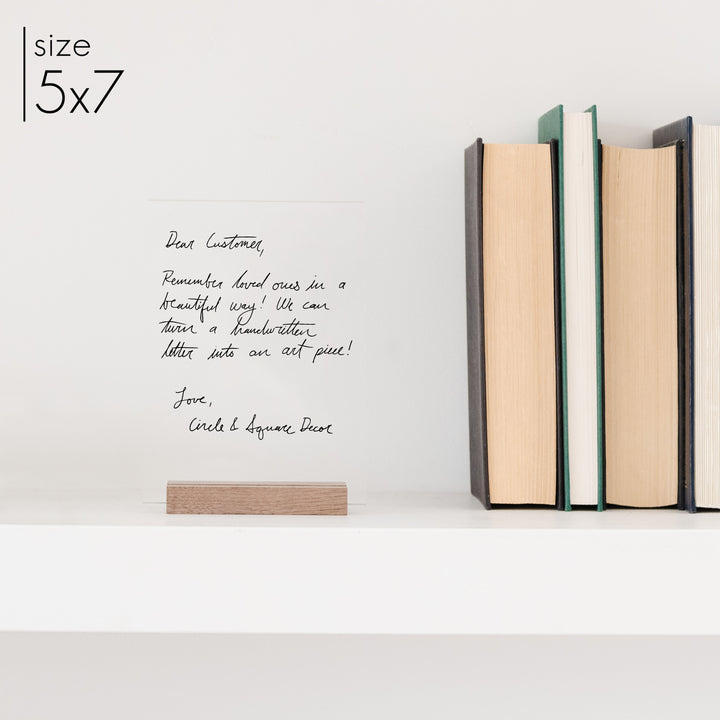 A 5x7 handwriting memorial printed on clear acrylic sitting on a wooden stand.