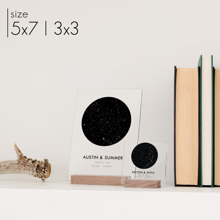Two customized acrylic wedding decor star charts with bold font titles on a bookshelf.