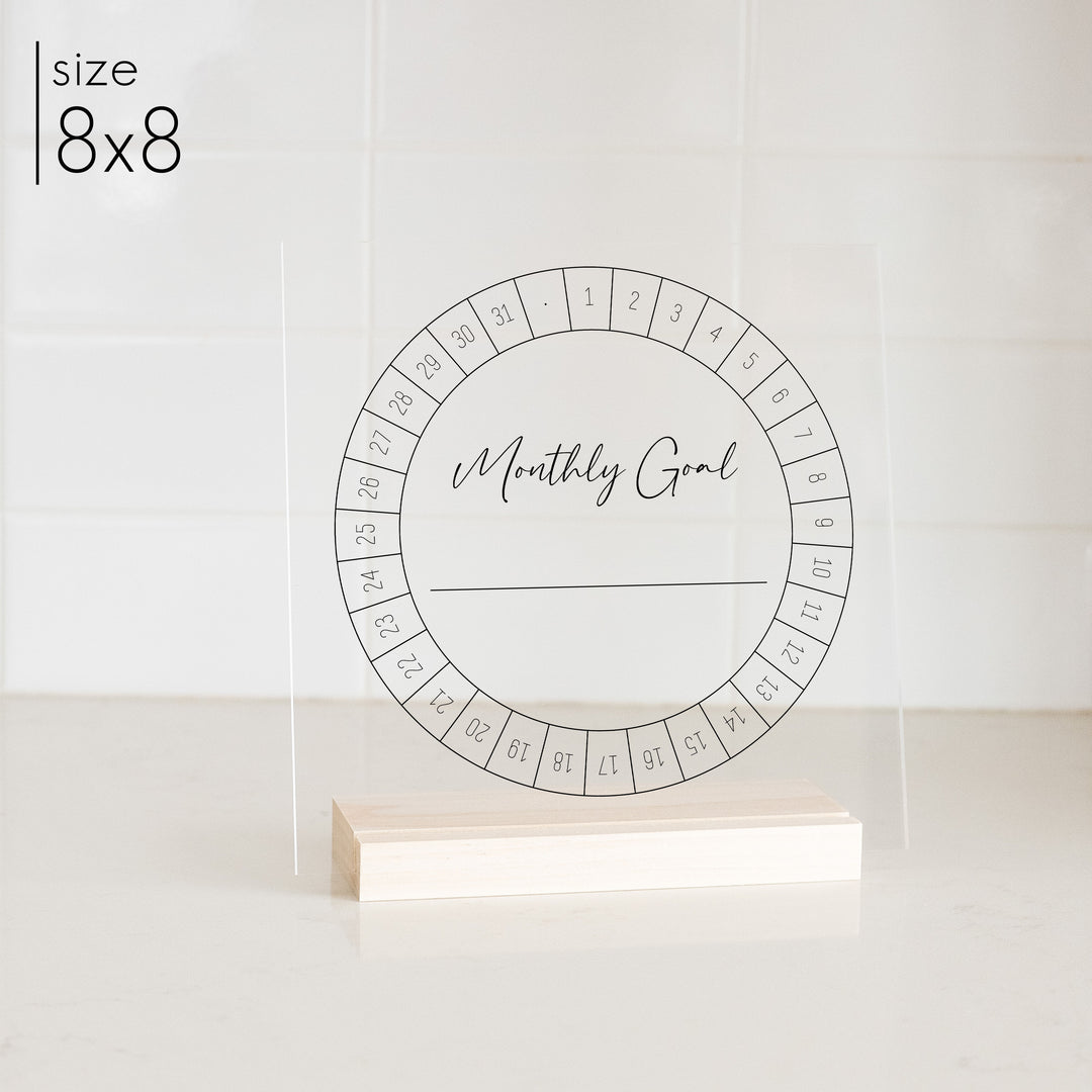 An 8x8 acrylic monthly goal tracker on a kitchen counter.